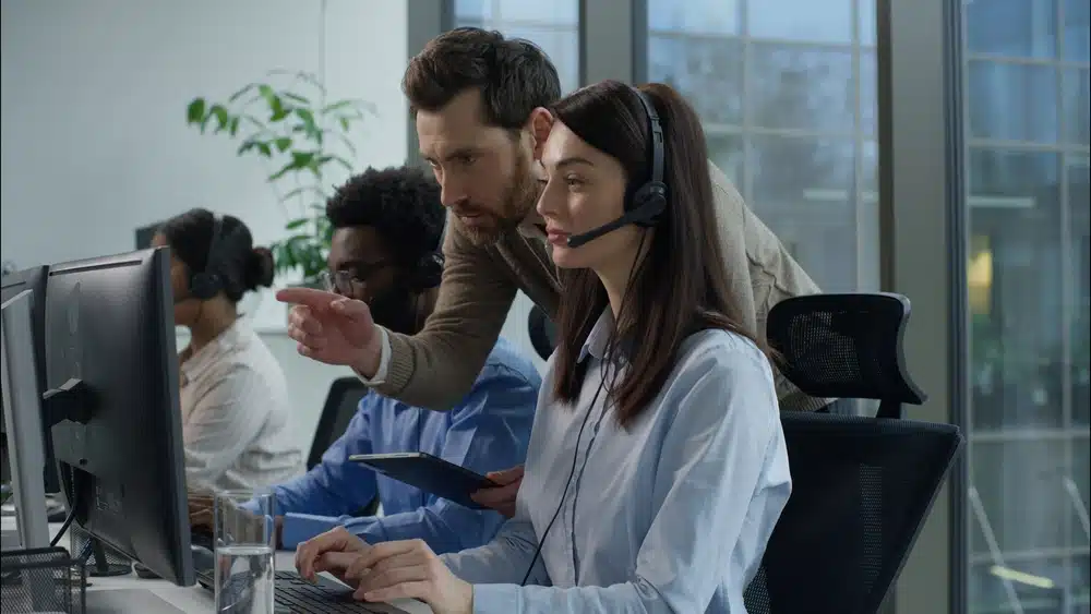 A man and woman work diligently at computers in a busy call center environment.