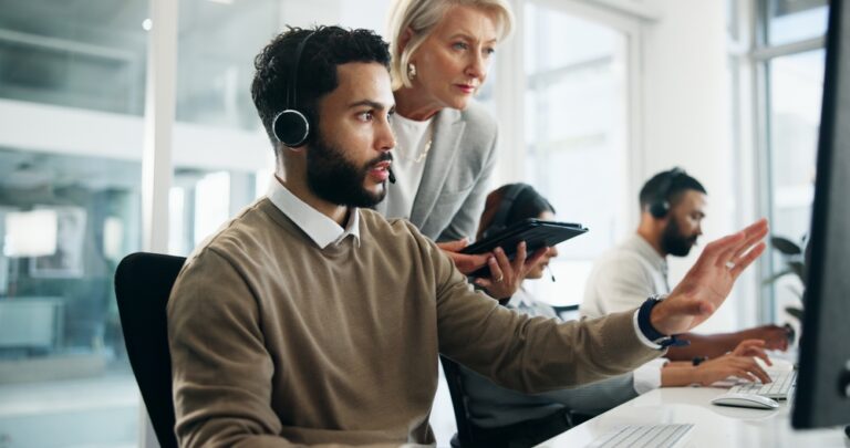 A man and woman work together at computers in a busy call center, focused on their tasks.