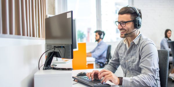 Friendly service agent using computer and talking to customer in call centre